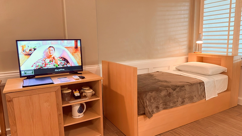 Fourplex Room single bed beside the window with TV and amenities console