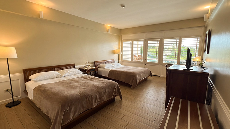 Two queen beds in the Upper-Floor Beachside Room with shuttered balcony doors