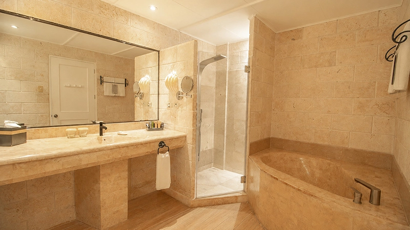 Water's Edge Room stone bathroom with double vanity, glass shower, and corner soaking tub