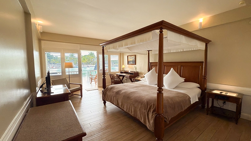 Canopied four-poster king bed in the Water's Edge Room with doors opening to the lagoon balcony